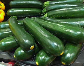 May include: A close-up of a basket filled with fresh, dark green zucchini. The zucchini are arranged in a variety of sizes and shapes, with some of them overlapping.