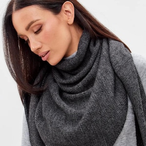 Peut inclure: Une écharpe gris foncé drapée autour du cou et des épaules. L'écharpe est faite d'une matière tricotée douce. La personne sur l'image porte un pull gris sous l'écharpe. L'écharpe semble être de couleur unie.