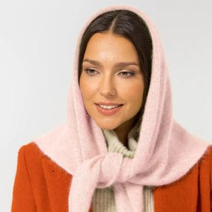 Peut inclure: Une femme portant une écharpe en tricot rose nouée autour de sa tête et de son cou. Elle porte une veste rouge et un pull blanc et vert en dessous.