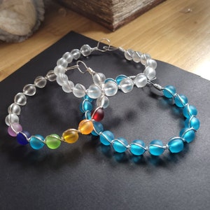 May include: Three wire-wrapped bracelets with frosted glass beads. The top bracelet has clear beads, the middle bracelet has rainbow colored beads, and the bottom bracelet has blue beads.
