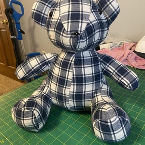 May include: A handmade teddy bear made from navy blue and white plaid fabric. The bear has black button eyes and is sitting on a green cutting mat. The bear's arms and legs are outstretched.