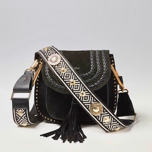 May include: Black suede shoulder bag with a black and white patterned strap featuring gold accents. The bag has a flap closure and a tassel.