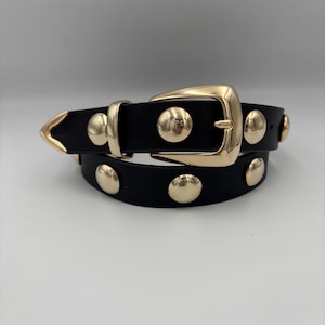 May include: A black leather belt with gold-toned studs and a buckle. The belt is rolled up and the buckle is facing the camera.