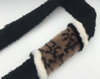 May include: A black and brown faux fur scarf with a white stripe. The scarf has a leopard print pattern.