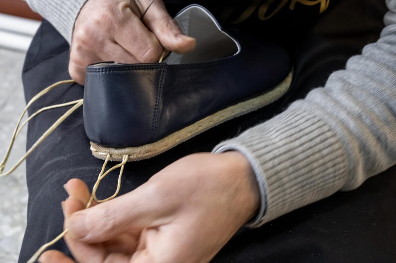 A person's hands are shown tying the laces of a black shoe, with the shoe partially visible in the background.