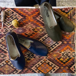 a pair of blue shoes, a pair of black shoes, and some crafting tools such as scissors and a needle, all placed on a colorful, patterned rug.