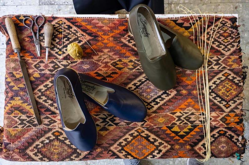 a pair of blue shoes, a pair of black shoes, and some crafting tools such as scissors and a needle, all placed on a colorful, patterned rug.