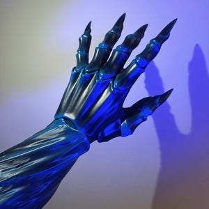 May include: A blue and black skeletal hand with long, sharp claws. The hand is posed against a gradient background, with a blue light source casting a shadow. The fingers are articulated, and the overall effect is eerie.