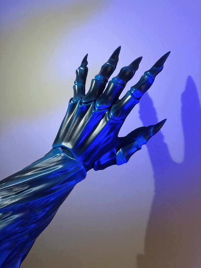 May include: A blue and black skeletal hand with long, sharp claws. The hand is posed against a gradient background, with a blue light source casting a shadow. The fingers are articulated, and the overall effect is eerie.