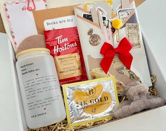 May include: A gift box containing a frosted glass tumbler with book-lover text, a Tim Hortons French Vanilla cappuccino packet, a 24K gold eye mask packet, a red bow, a notepad with cherry print, a gold metal pendant, and a fuzzy gray hair claw clip.