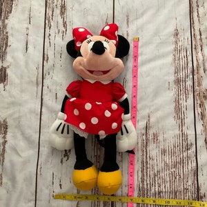 May include: A Minnie Mouse plush doll, featuring a red dress with white polka dots and a matching bow. The doll has black ears, a pink face, and yellow shoes. The doll is approximately 13 inches tall.