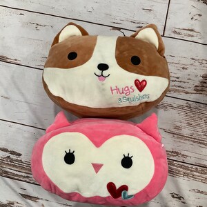 Puede incluir: Dos peluches, un perro marrón y blanco y un búho rosa y blanco, con corazones bordados y el texto "Hugs & Squishes".