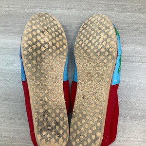 May include: Pair of red, blue, and green canvas shoes. The soles are light brown with a dotted pattern. The toe and heel are red, while the top of the shoe is blue and green. The shoes appear worn.