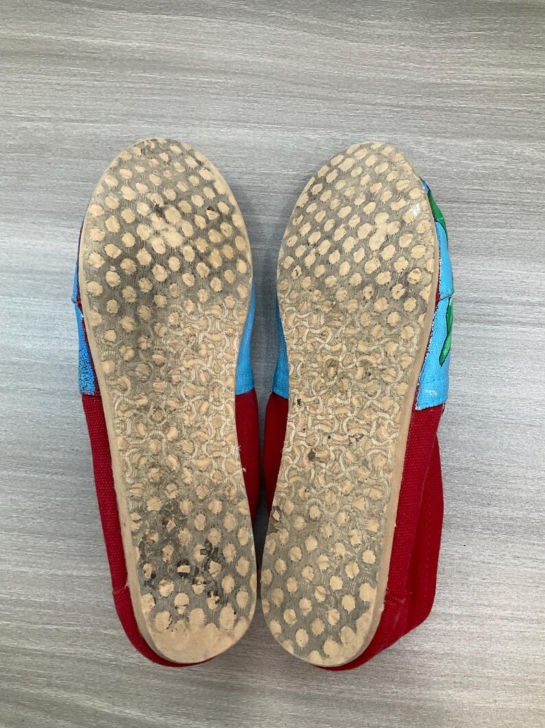 May include: Pair of red, blue, and green canvas shoes. The soles are light brown with a dotted pattern. The toe and heel are red, while the top of the shoe is blue and green. The shoes appear worn.