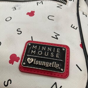 May include: White backpack with a pattern of black letters and red Minnie Mouse silhouettes. A rectangular black and red patch reads "MINNIE MOUSE" and "loungefly" in silver lettering.