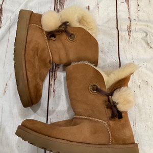May include: A pair of brown suede boots with faux fur trim and a pom-pom detail on the laces.