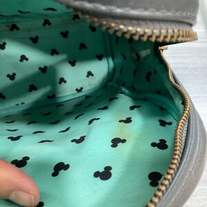 May include: Gray zippered bag with a teal interior patterned with black Mickey Mouse silhouettes. The bag's interior shows some discoloration. The zipper is a brass color.