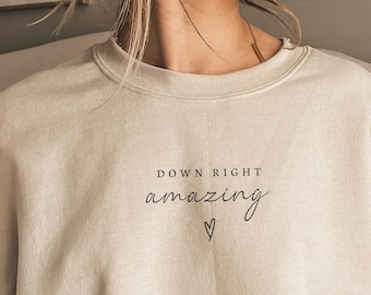 May include: A beige sweatshirt with the text "Down Right Amazing" and a small heart graphic printed on the front.