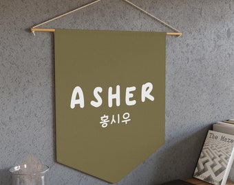 May include: A brown pennant banner with the name "ASHER" in white text and the Korean word for "Hope" in white text below. The banner is hanging from a wooden dowel rod.