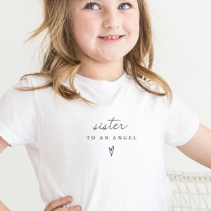 May include: A white t-shirt with the text "sister to an angel" and a small heart.