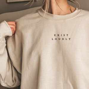 May include: A beige sweatshirt with the text "EXIST LOUDLY" printed on the front.