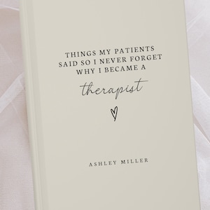 May include: A cream-colored journal with the text "THINGS MY PATIENTS SAID SO I NEVER FORGET WHY I BECAME A therapist" in black script. A small heart symbol is below the word "therapist". The author's name, Ashley Miller, is at the bottom.