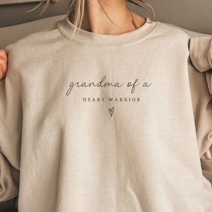 May include: A beige sweatshirt with the text "grandma of a heart warrior" and a small heart symbol.