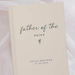 May include: A cream-colored book with the text "father of the bride" in elegant script. Below, the word "bride" is centered, with a heart symbol beneath it. The names "Kayla and Evan" and the date "11.22.2025" are printed at the bottom.