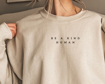 May include: A beige sweatshirt with the text "BE A KIND HUMAN" printed on the front.
