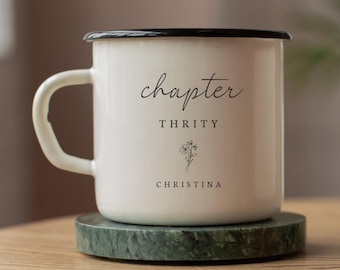 May include: White enamel mug with a black rim and handle, resting on a green marble coaster. The mug features the word "chapter", "THRITY", a floral illustration, and the name "CHRISTINA" in black script.