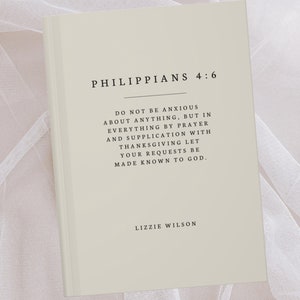 May include: A beige book with the text "Philippians 4:6" and a quote from the Bible verse. The quote reads "Do not be anxious about anything, but in everything by prayer and supplication with thanksgiving let your requests be made known to God." The book is signed "Lizzie Wilson".