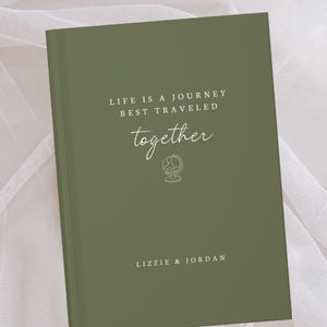 May include: An olive green journal with the words "LIFE IS A JOURNEY BEST TRAVELED together" in white script. A globe icon is below the word "together". The names "LIZZIE & JORDAN" are printed at the bottom.