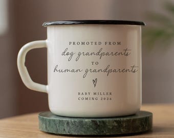 May include: White enamel mug with black rim and handle. The mug has the text "PROMOTED FROM dog grandparents TO human grandparents" with a heart symbol and "BABY MILLER COMING 2026" in black script. The mug sits on a green marble coaster.