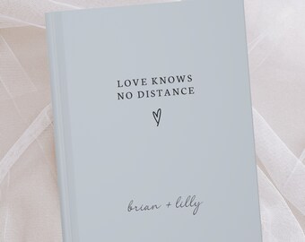 May include: A light blue journal with the text "LOVE KNOWS NO DISTANCE" and a small heart symbol. The names "brian + lilly" are written below the text.