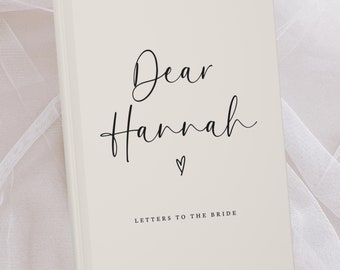 May include: A white book with the text "Dear Hannah" in black cursive writing and a small heart symbol. The text "Letters to the Bride" is printed below the name.