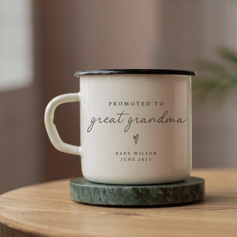 May include: White enamel mug with a black rim and handle. The mug has the text "Promoted to great grandma" with a heart symbol and the text "Baby Wilson June 2025".
