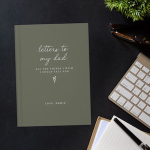 May include: A green journal with the text "letters to my dad" and "ALL THE THINGS I WISH I COULD TELL YOU" in white. A small heart symbol is below the text. The text "LOVE, EMMIE" is at the bottom of the journal.