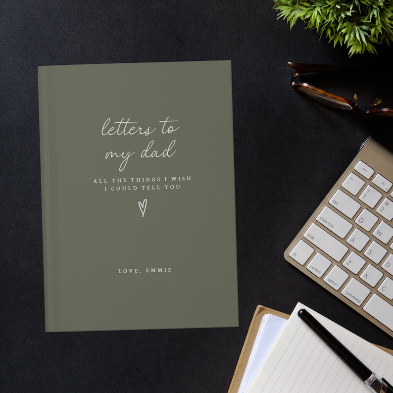 May include: A green journal with the text "letters to my dad" and "ALL THE THINGS I WISH I COULD TELL YOU" in white. A small heart symbol is below the text. The text "LOVE, EMMIE" is at the bottom of the journal.