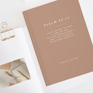 May include: A brown notebook with the text "PSALM 86:12" and a bible verse printed in white. The notebook has the name "ASHLEY TAYLOR" printed at the bottom.