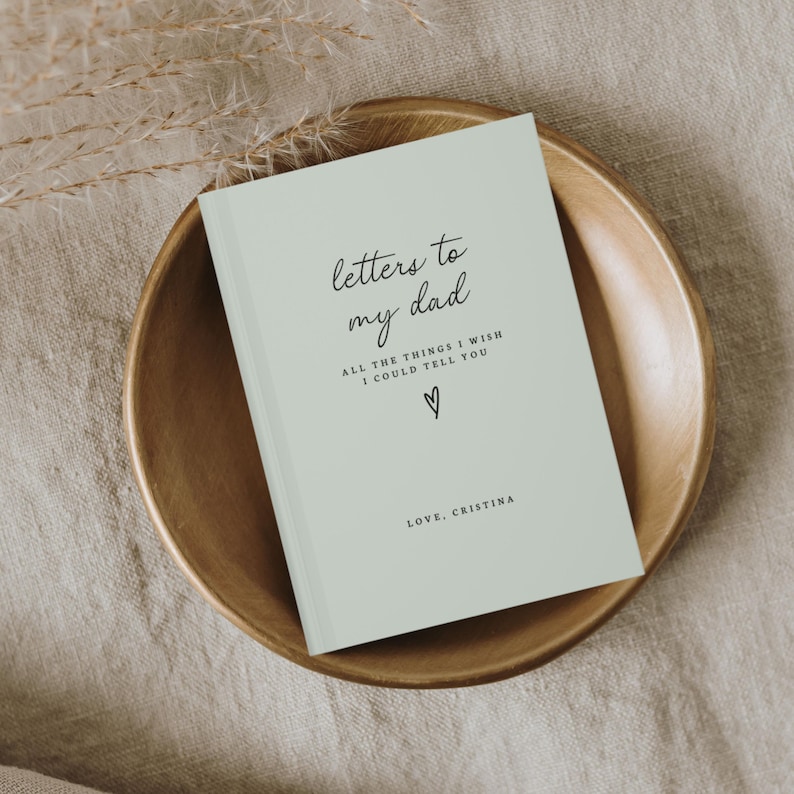May include: A light green journal with the text "letters to my dad" and "ALL THE THINGS I WISH I COULD TELL YOU" in black script. A small heart symbol is below the text. The text "LOVE, CRISTINA" is at the bottom of the journal.
