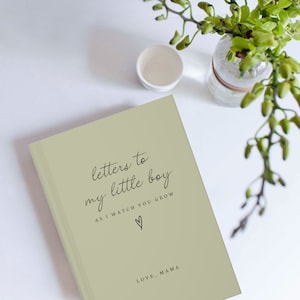 May include: A sage green journal with the text "letters to my little boy as I watch you grow" and a heart symbol. The text "love, mama" is at the bottom of the journal.