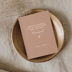 May include: A hardcover journal with a muted rose-colored cover, resting in a wooden bowl. The cover features the text "THINGS MY PATIENTS SAID SO I NEVER FORGET WHY I BECAME A therapist" with a heart symbol and the name "KIERA JOHNSON".