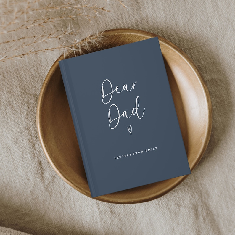 May include: A dark blue hardcover book with white text on the front cover that reads Dear Dad with a small heart icon below it and the text LETTERS FROM EMILY printed in a smaller font at the bottom of the cover, featuring a clean design.