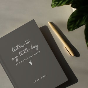 May include: A gray journal with the text "letters to my little boy as I watch you grow" and a heart symbol. The text "LOVE, MOM" is at the bottom of the journal.