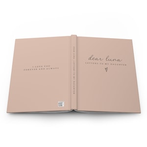 May include: Open journal with a light pink cover. The left page reads "I LOVE YOU FOREVER AND ALWAYS." The right page says "dear luna LETTERS TO MY DAUGHTER" with a heart symbol. The spine reads "DEAR LUNA | LETTERS TO MY DAUGHTER."