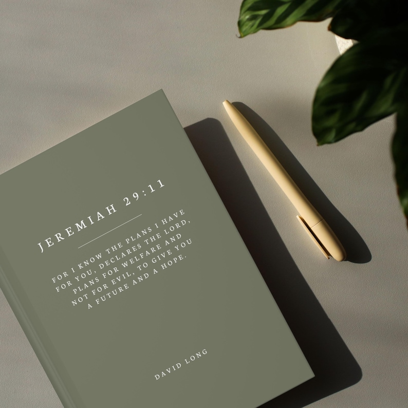 May include: A sage green journal with the text "JEREMIAH 29:11" and a quote from the Bible verse. The quote reads "For I know the plans I have for you, declares the Lord, plans for welfare and not for evil, to give you a future and a hope." The journal also has the text "DAVID LONG" at the bottom.