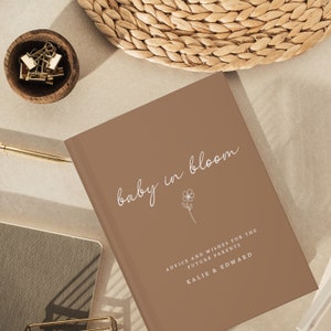 May include: A brown book with the text "baby in bloom" in white script. The book has the text "Advice and wishes for the future parents Kalie & Edward" in white text.