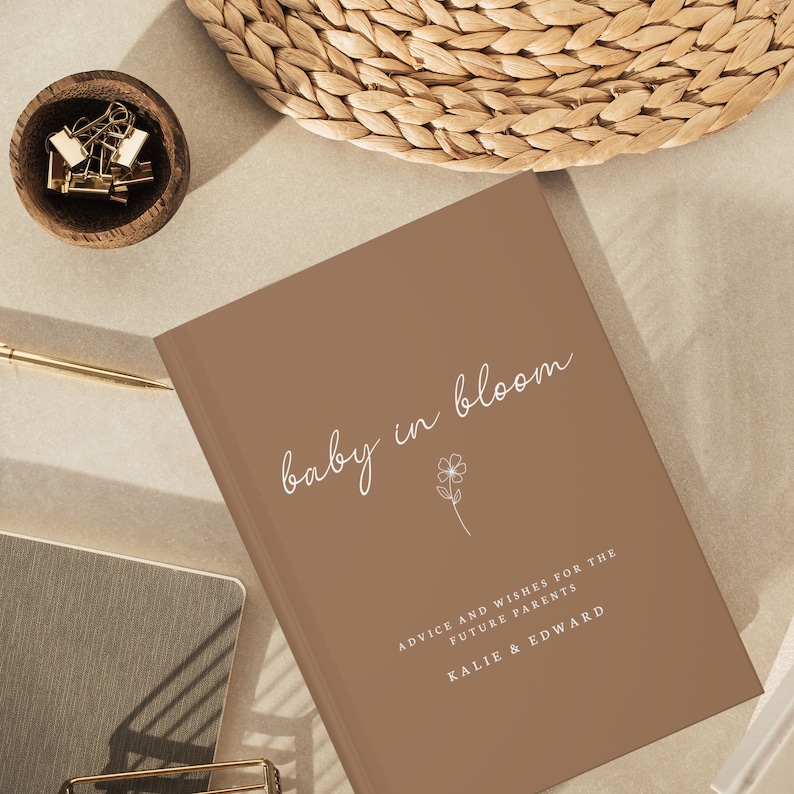 May include: A brown book with the text "baby in bloom" in white script. The book has the text "Advice and wishes for the future parents Kalie & Edward" in white text.