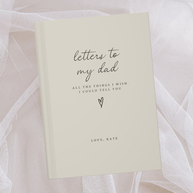 May include: A beige journal with the text "letters to my dad" and "ALL THE THINGS I WISH I COULD TELL YOU" in black script. A small heart symbol is below the text. The text "LOVE, KATE" is at the bottom of the journal.