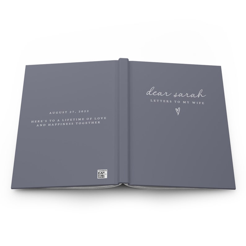 May include: Open journal with a gray cover. The left page has the date "August 27, 2022" and the text "Here's to a lifetime of love and happiness together." The right page reads "dear sarah LETTERS TO MY WIFE" with a heart symbol.